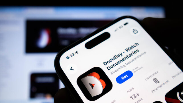 Closeup of a smartphone screen displaying the docubay app page on the apple app store, held in a hand in a dimly lit room