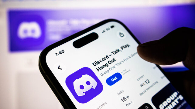 Closeup of a hand holding a smartphone displaying the discord app page on the apple app store, showing the logo and download button