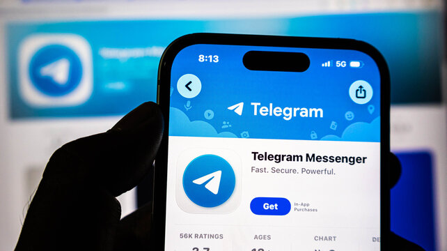 Closeup of a hand holding a smartphone displaying the telegram messenger app store page on a screen
