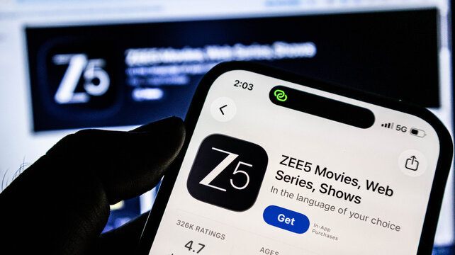 Closeup of a person holding a smartphone displaying the zee5 mobile application on the apple app store, showcasing movies and web series
