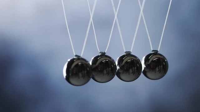 A close up view of a Newtons cradle demonstrates conservation of momentum and energy as metal spheres swing in dynamic motion.