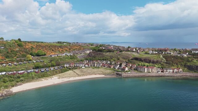 Aerial cinematic drone sideward tracking shot of Pettycur Bay sandy beach, waterfront houses and holiday caravan park, Fife, Scotland.
