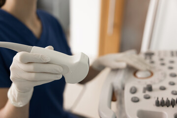 Fototapeta premium Closeup of female medical sonographer specialist in scrubs and gloves holding transducer probe, using ultrasound imaging machine during procedure at hospital. Examination and diagnostics services