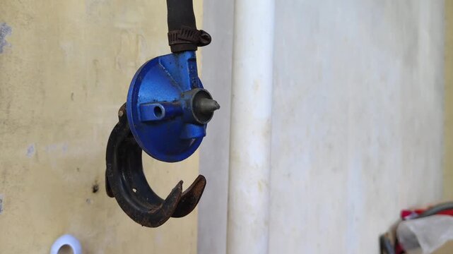 Close-up of a blue gas regulator valve with rusty metal hook for LPG gas stove. Industrial gas equipment showing wear and tear, commonly used for kitchen cooking gas connection.