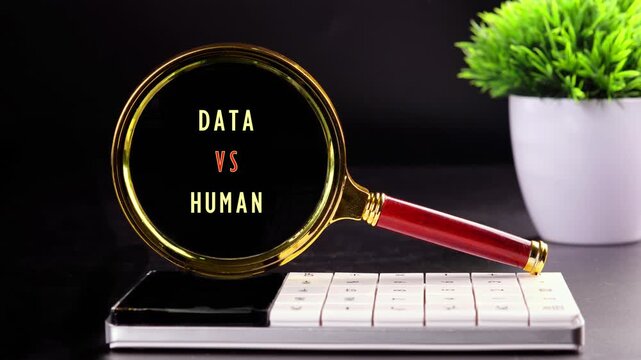 A golden magnifying glass reveals the words DATA VERSUS HUMAN on a white computer keyboard. This concept is displayed on a dark desk next to a green potted plant