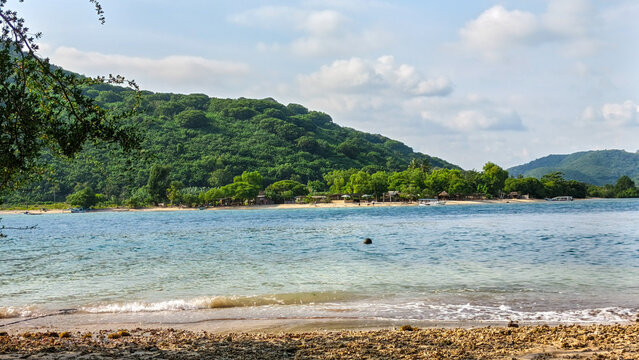 Tropical beach landscape at gili island. Beautiful caribbean coasline with crystal clear blue water and dense jungle mountain. Small wooden boats and beach huts visible along the tropical shoreline.
