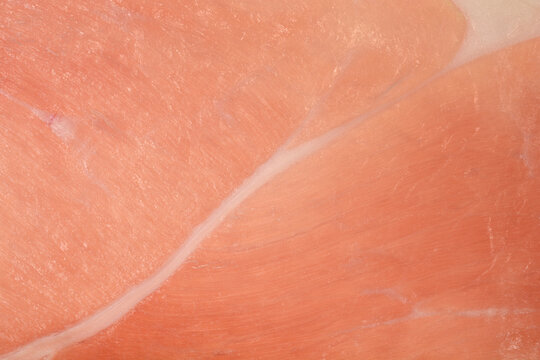 Full frame macro view of a slice of raw cured prosciutto ham showing a thin white fat line and lean pink meat texture.