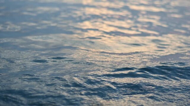Close up nature background of blue water surface in the sea with little waves breaking to the beach under sunlight. Near focal length.