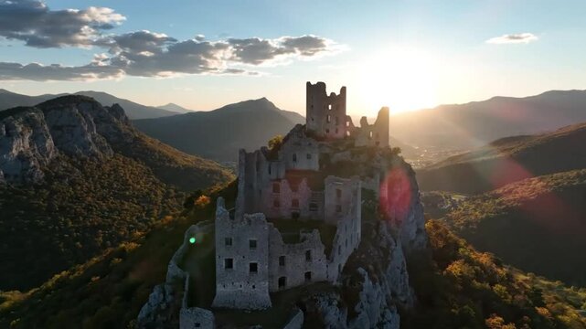 Epic aerial view of a medieval castle ruin silhouetted against a setting sun over scenic mountains