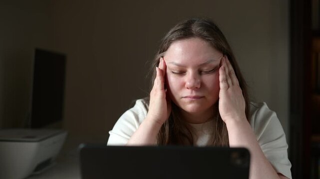 Tired woman massaging temples while working on laptop at home