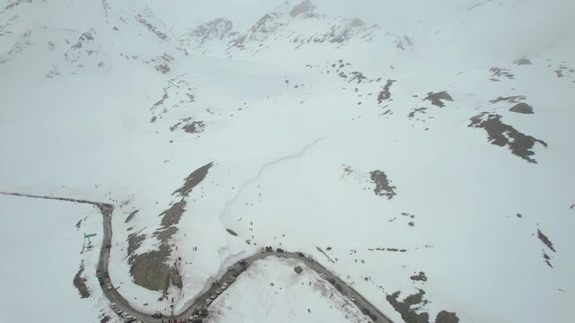 Aerial drone panning up showing tourists enjoying snow amidst Himalaya mountains with the Shingo La pass road winding off in the distance and 4X4 cars parked nearby showing the beauty of Ladakh Leh In