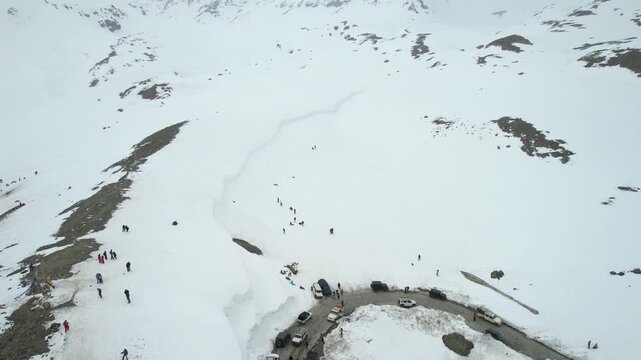 Aerial drone orbit wide view of tourists exploring snowy mountains near Shinkula Top Pass Sissu with parked 4X4 vehicles on winding roads in Ladakh Himachal Pradesh India during winter