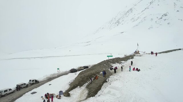 Aerial drone moving to tourists climbing stairs to Sinkula Top hill surrounded by snow covered mountains with the 4X4 cars parked nearby showing the beauty of Ladakh Leh India