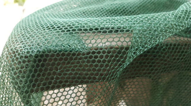 Detailed texture of lightweight breathable green polyester mesh fabric with a geometric hexagonal honeycomb pattern suitable for athletic sportswear design and textile industry manufacturing.