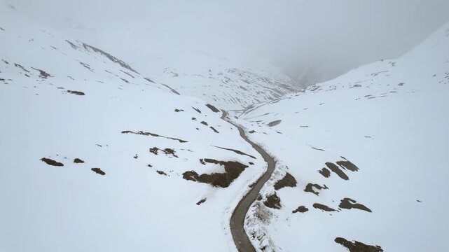 Aerial drone moving back showing the Shingo La Pass road amid snow covered Himalaya mountains during snow fall showing the cold and beautiful environments of Ladakh, Leh, Sissu and Himachal Pradesh