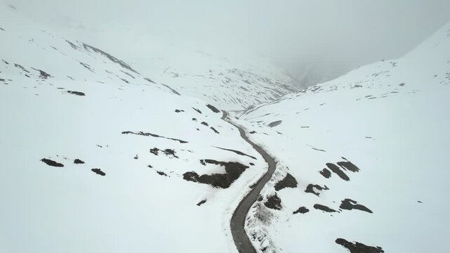 Aerial drone moving back showing the Shingo La Pass road amid snow covered Himalaya mountains during snow fall showing the cold and beautiful environments of Ladakh, Leh, Sissu and Himachal Pradesh