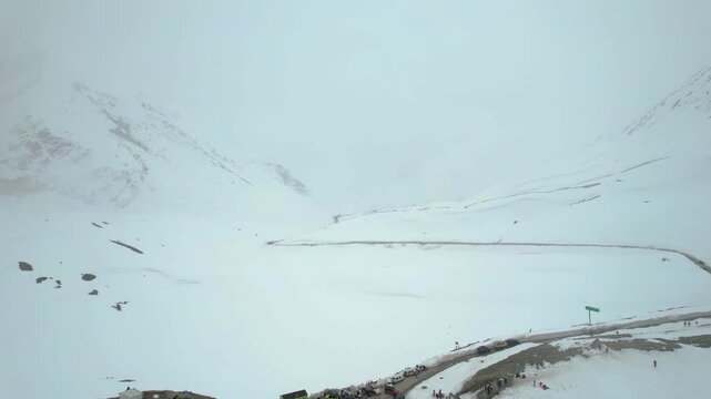 Aerial drone shot descend fly to crowd of people and 4X4 car bus parking to show snow covered surroundings winding roads and mountains of Shinkula top pass in Sissu Ladakh Himachal Pradesh