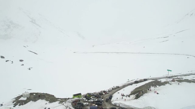 Aerial dronie shot flying away from crowded 4X4 car bus parking to show snow covered surroundings winding roads and mountains of Shinkula top pass in Sissu Ladakh Himachal Pradesh