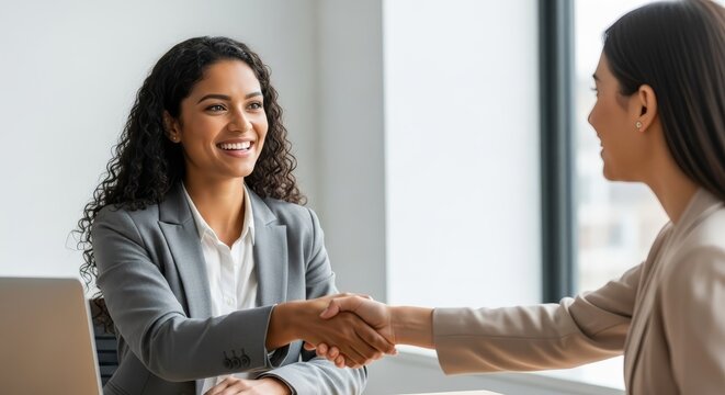 Smiling woman in a professional business handshake in an office setting, celebrating a new agreement and opportunity.
