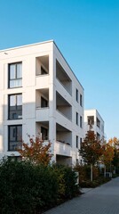 Fototapeta premium Modern White Apartment Building with Balconies and Trees Under a Clear Blue Sky.