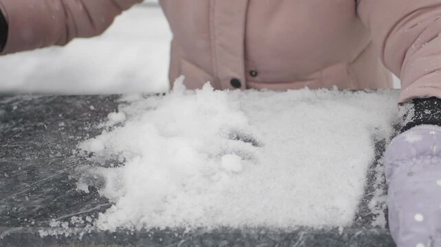 child hands pack snow on a table outside during wintertime in a snowy area