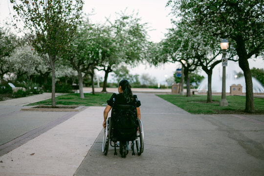 Woman in a wheelchair moving along a path in a park