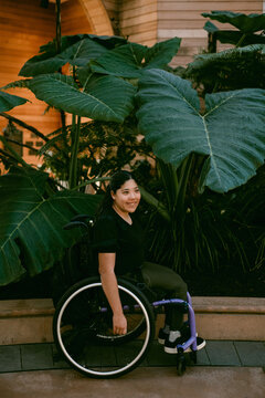Smiling young woman in wheelchair outdoors with plants