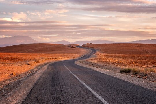 Winding empty road through a desert landscape at sunset in Morocco