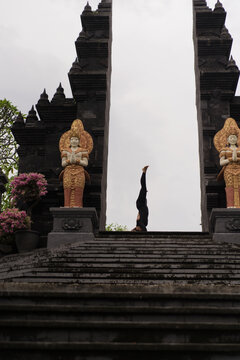 Woman doing headstand above Balinese temple gate with statues, Bali