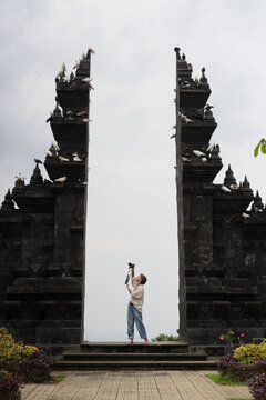 Woman photographer shooting flying doves at Balinese temple gate