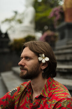 Bearded man with frangipani flower in hair at Balinese temple, Bali