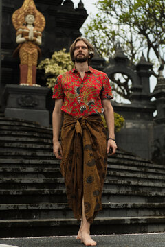 Confident man in batik shirt and sarong at Balinese temple steps, Bali