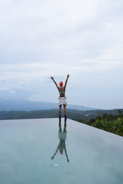 Woman with arms raised at infinity pool above clouds, Munduk, Bali