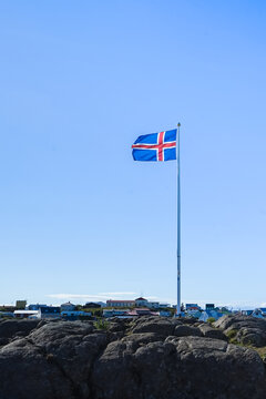 Icelandic flag flying high on a rocky outcrop against a clear blue sky,Iceland