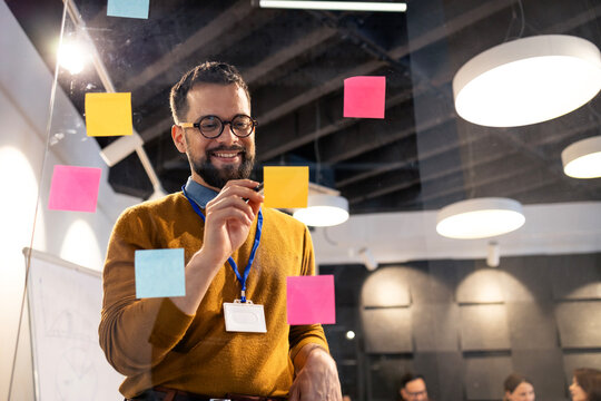 Employee in a meeting writing on sticky notes on a glass board, brainstorming and collaborating on new business strategy