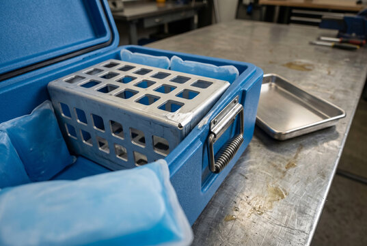 High angle view of a perforated anodized aluminum laboratory rack inside an open cooling box. A fresh metallic scrape mark highlights the material interactions and the high-value nature of industrial 