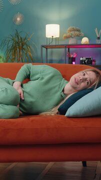 Sick ill woman suffering from period cramps, painful stomach ache lying on sofa at home room. lady holding belly, feeling abdominal or menstrual pain. Abdominal pain, gastritis, diarrhea, indigestion