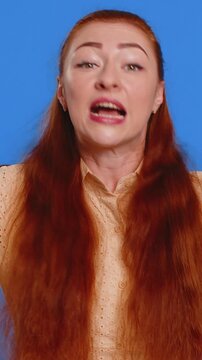 Quarrel. Displeased young adult woman gesturing hands with irritation and displeasure, blaming scolding for failure asking why this happened. Redhead attractive lady isolated on blue studio background