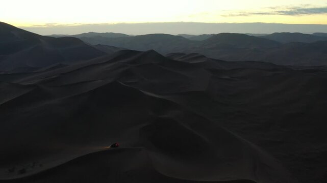 Off-road vehicle driving through desert sand dunes at sunset