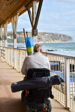 Man on a mobility scooter taking his chair and windbreak to the beach in Swanage UK able to enjoy a day on the beach despite his disability as the vehicle allows him to be independent and travel freel