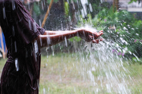 A person's hand catches heavy rainwater outdoors with a blurred green lawn background.