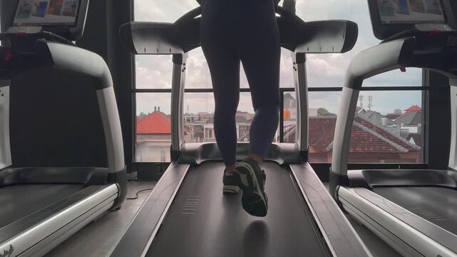 A  woman figure is walking on a treadmill shot from behind