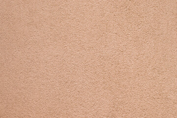 Detailed rough texture of a solid concrete wall painted in warm peach tones. © Rio