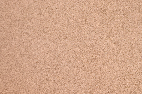 Detailed rough texture of a solid concrete wall painted in warm peach tones.