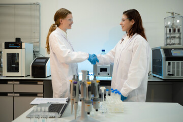 Naklejka premium Two Female Scientists Shaking Hands in Modern Research Laboratory with Equipment and Pipettes