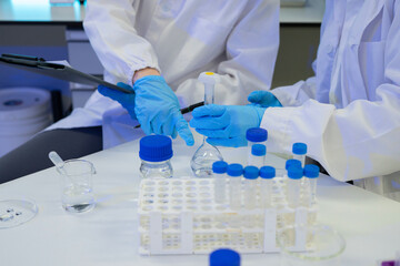 Fototapeta premium Scientists in Lab Coats and Blue Gloves Conducting Chemical Experiment with Flasks and Sample Vials
