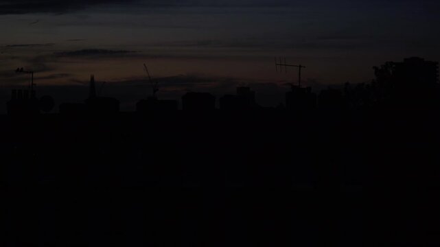 Footage captured from indoors through a window, showing a deep red sunset sky above urban surroundings in London, England. The scene features city silhouettes, warm evening colors, and atmospheric lig