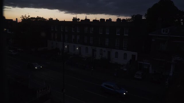 Footage captured from indoors through a window, showing a deep red sunset sky above urban surroundings in London, England. The scene features city silhouettes, warm evening colors, and atmospheric lig