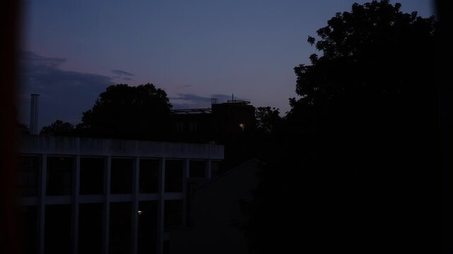 Footage captured from indoors through a window, showing a deep red sunset sky above urban surroundings in London, England. The scene features city silhouettes, warm evening colors, and atmospheric lig