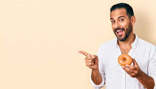 Hispanic young man enjoying a delicious donut, smiling and pointing for advertising design concept